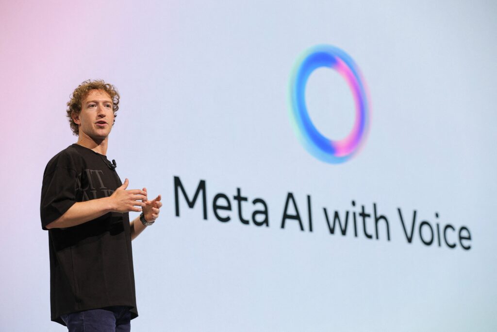 Mark Zuckerberg, CEO of Meta, speaking on stage during a presentation about Meta AI with Voice, with the Meta AI logo displayed on the screen behind him.